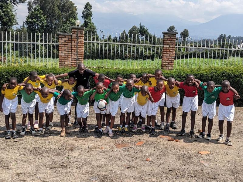 Pupils in yellow, green and red shirts standing in a long row with their arms around each other, an adult in black at the centre