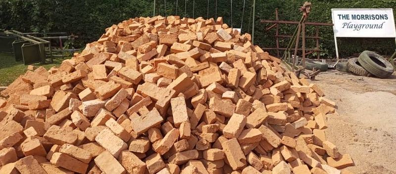 A large pile of red bricks beside a sign reading The Morrisons Playground