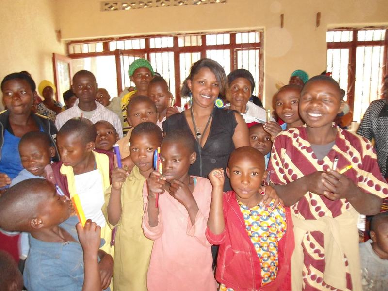 Smiling children and women crowded together inside a hall, some of the children holding pens