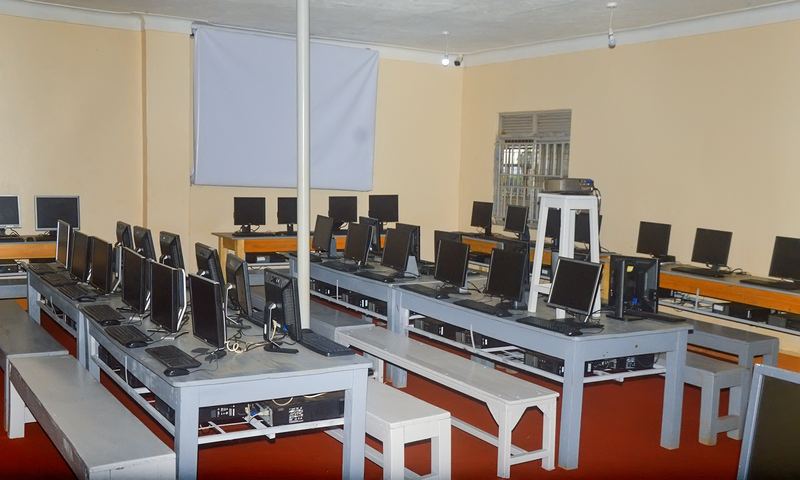 Illustrative image, not Faith Foundation: a computer room with rows of desktop computers on grey tables, wooden benches, a projector screen and a red floor