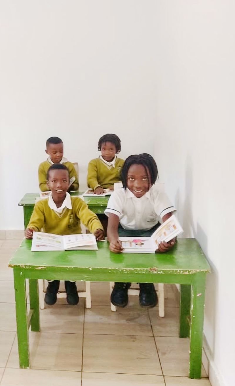 Four pupils smiling over open picture books at green desks in a white room