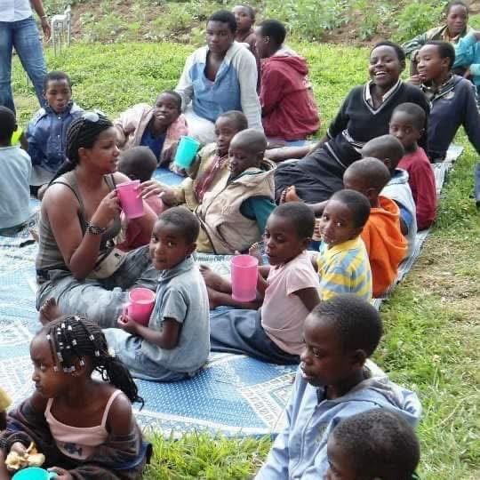 Faith Uwantege, the founder, sitting with children on mats on the grass, everyone holding coloured plastic cups