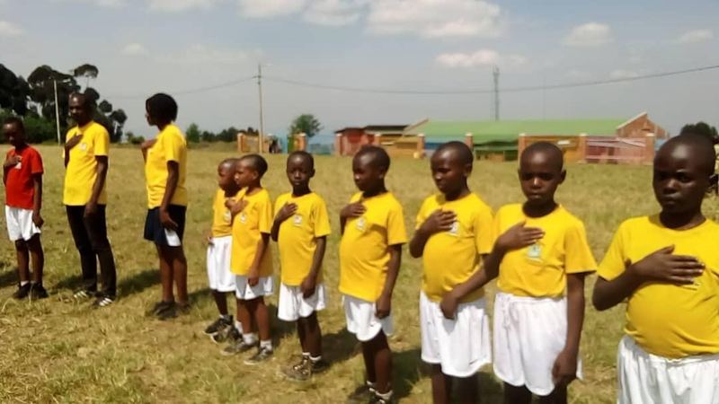 Pupils in yellow shirts and white shorts standing in a line with their hands on their chests